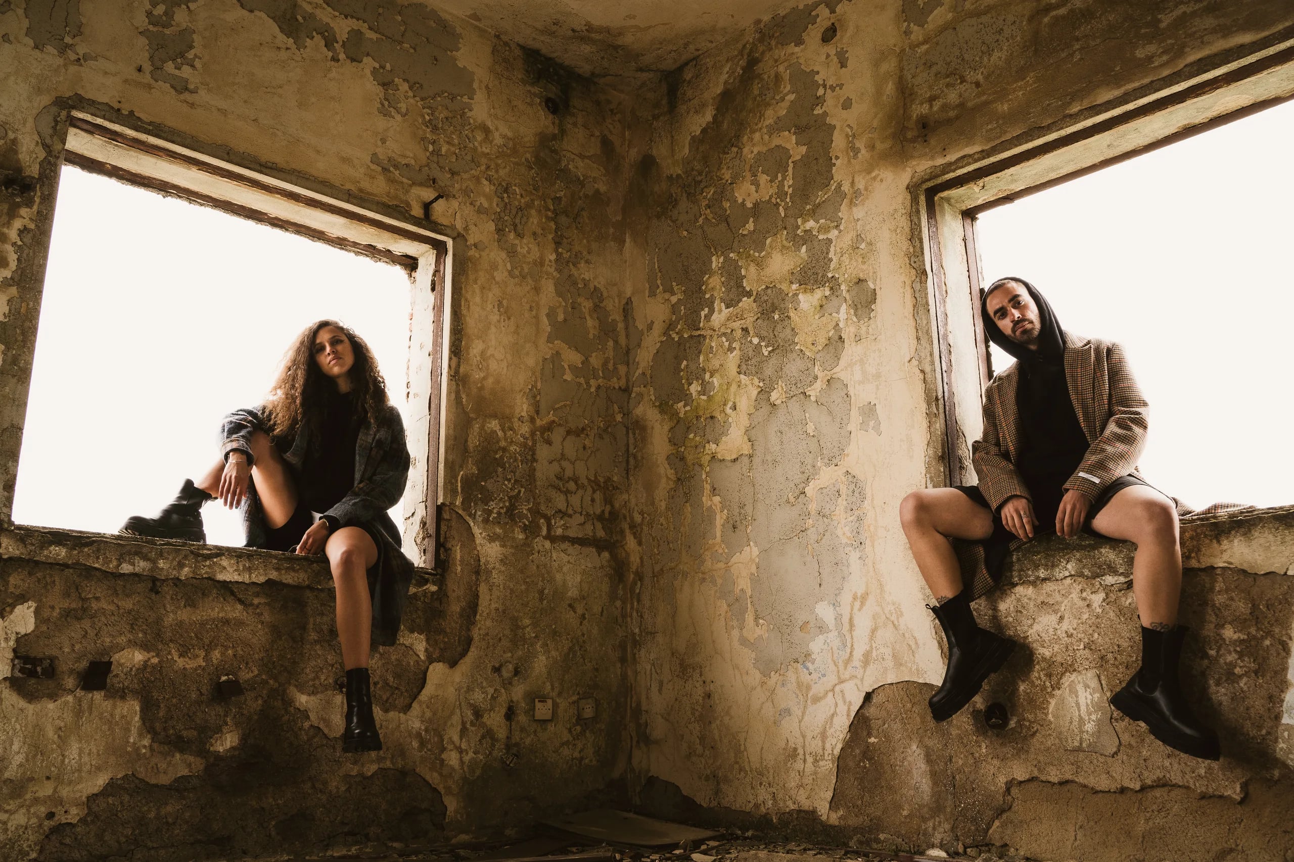 Two models posing in the windows of an abandoned building