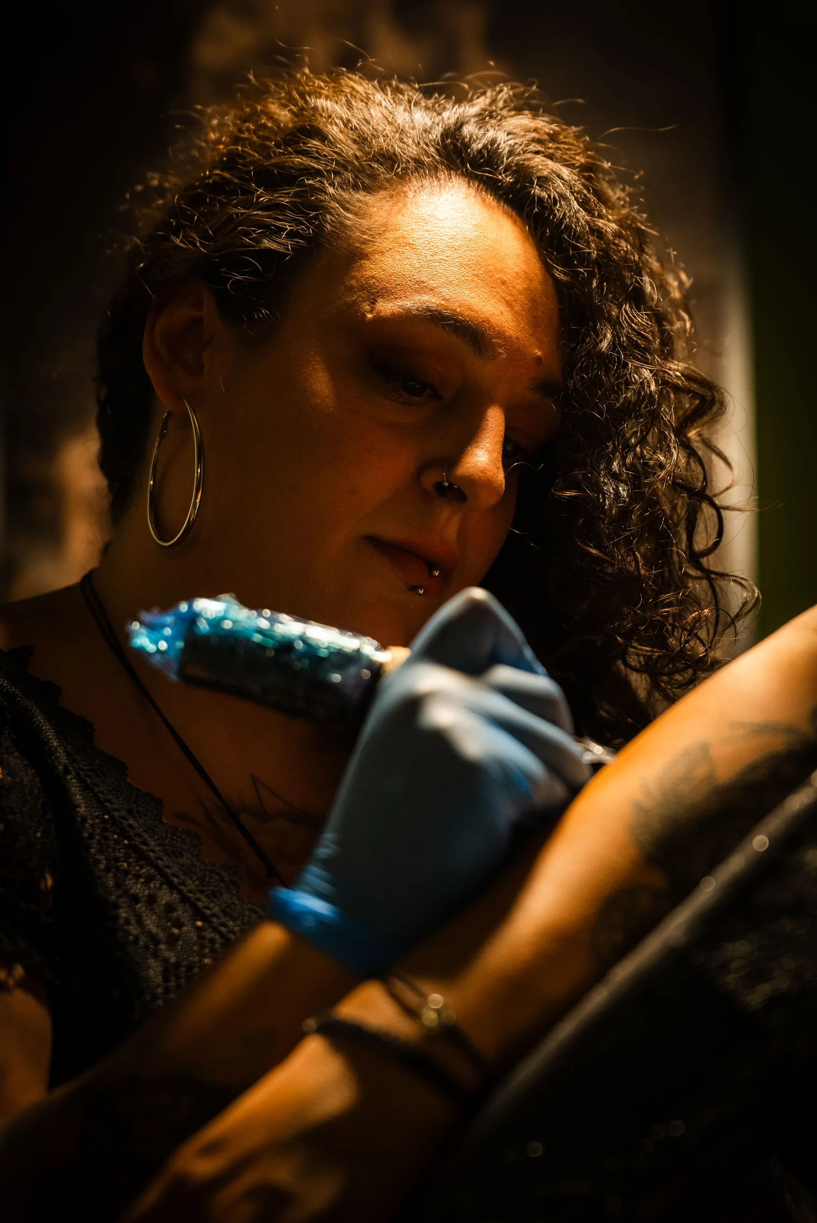 Tattoo artist with curly hair inking a client's arm
