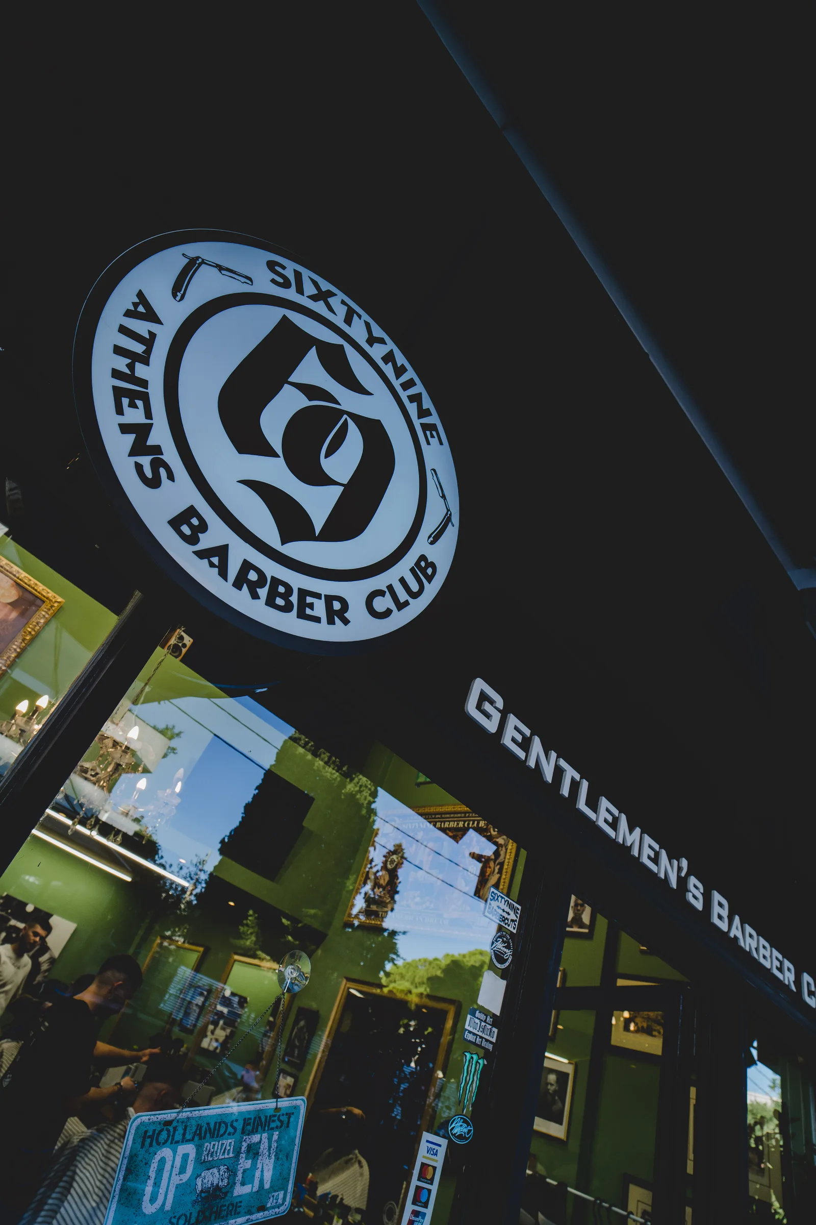 Lit sign of Athens Barber Club above the shop window