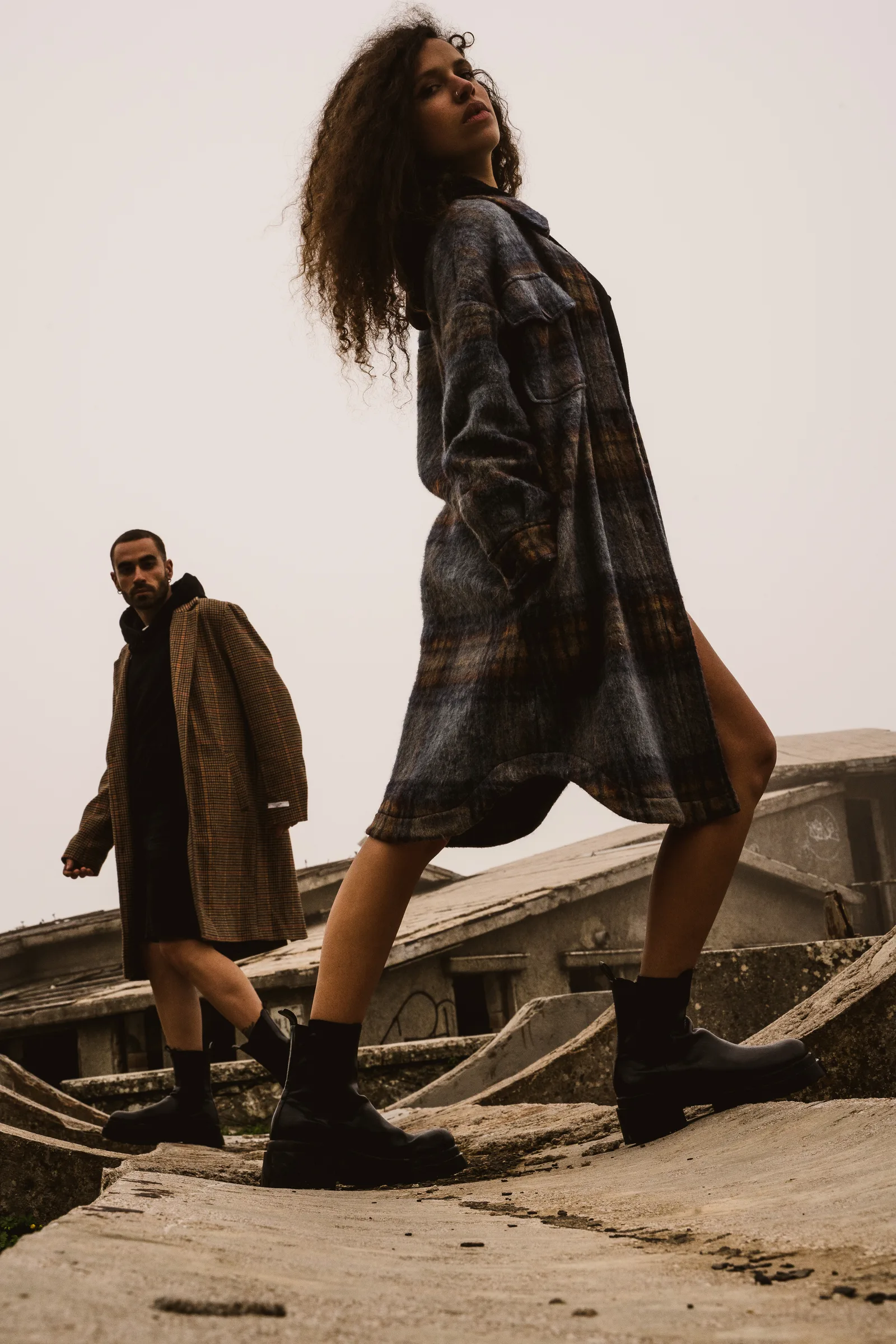 Two models in coats walking across concrete ruins